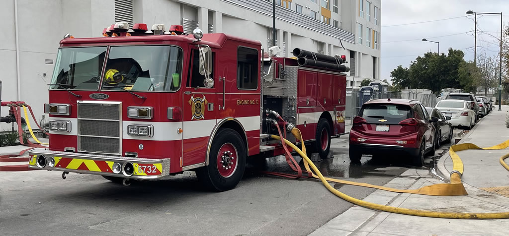 Red fire engine with hoses connected to a nearby building for test purposes.